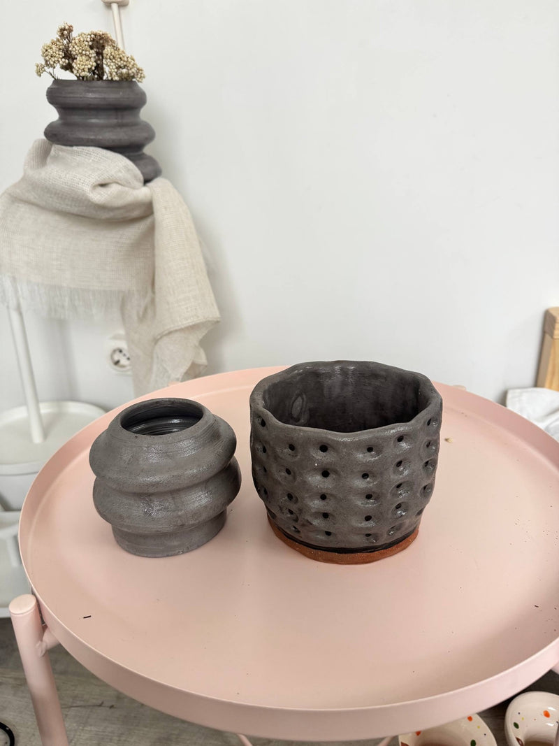 Two grey stoneware pieces on a pink table, one stacked, one pierced