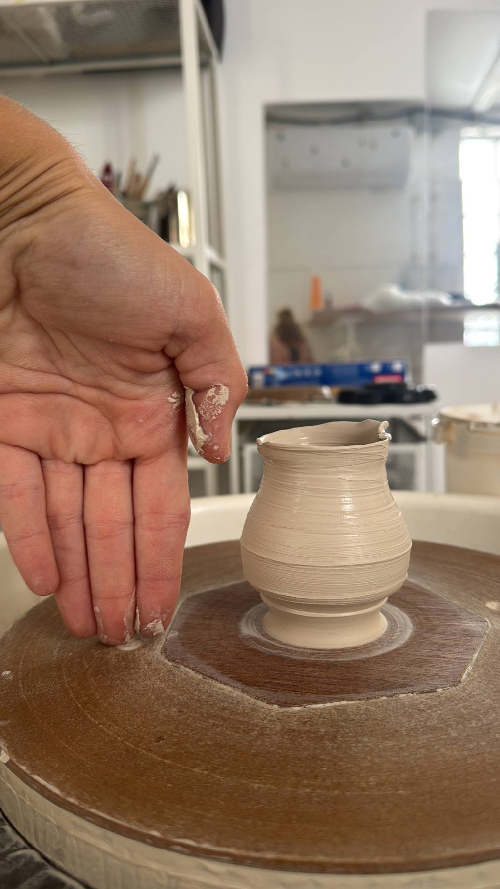 Maria's hand beside a freshly thrown vase on the pottery wheel