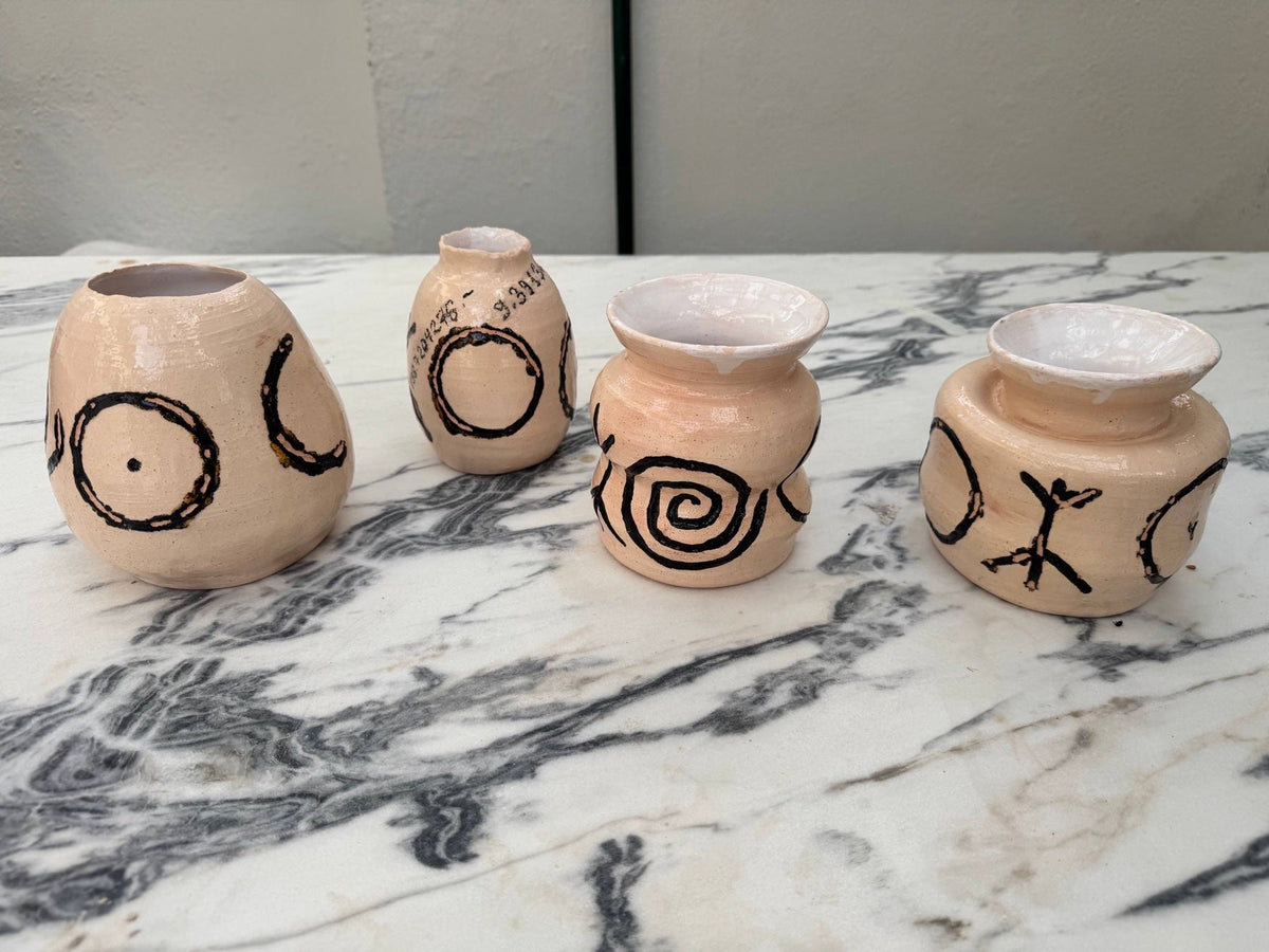 Four hand-painted vases with black symbols on a marble table