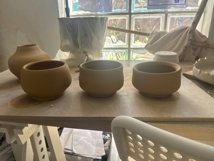 Unfired bowls drying slowly on a studio shelf